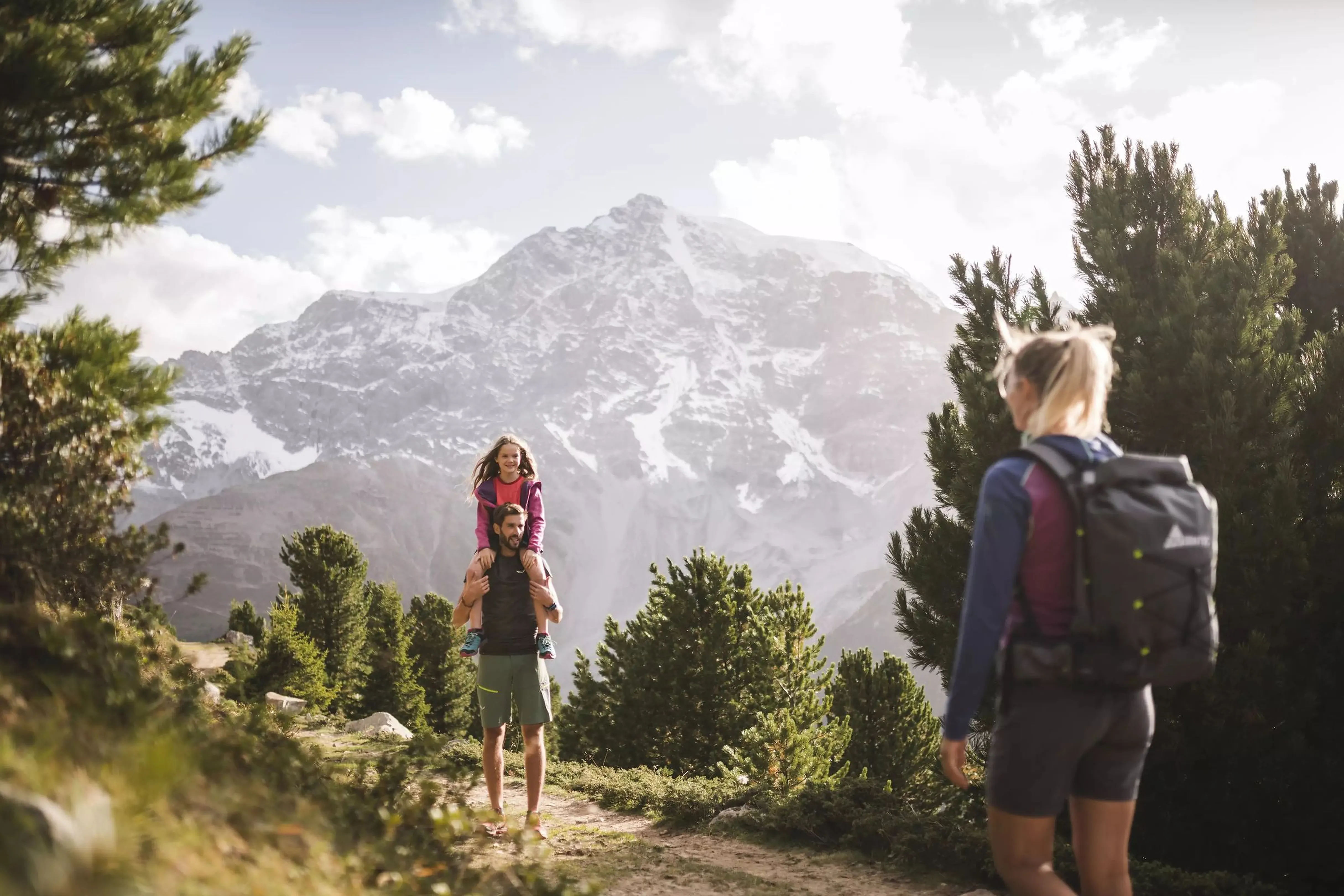 Familie wandert zwischen Zirben, dahinter das Ortler-Massiv