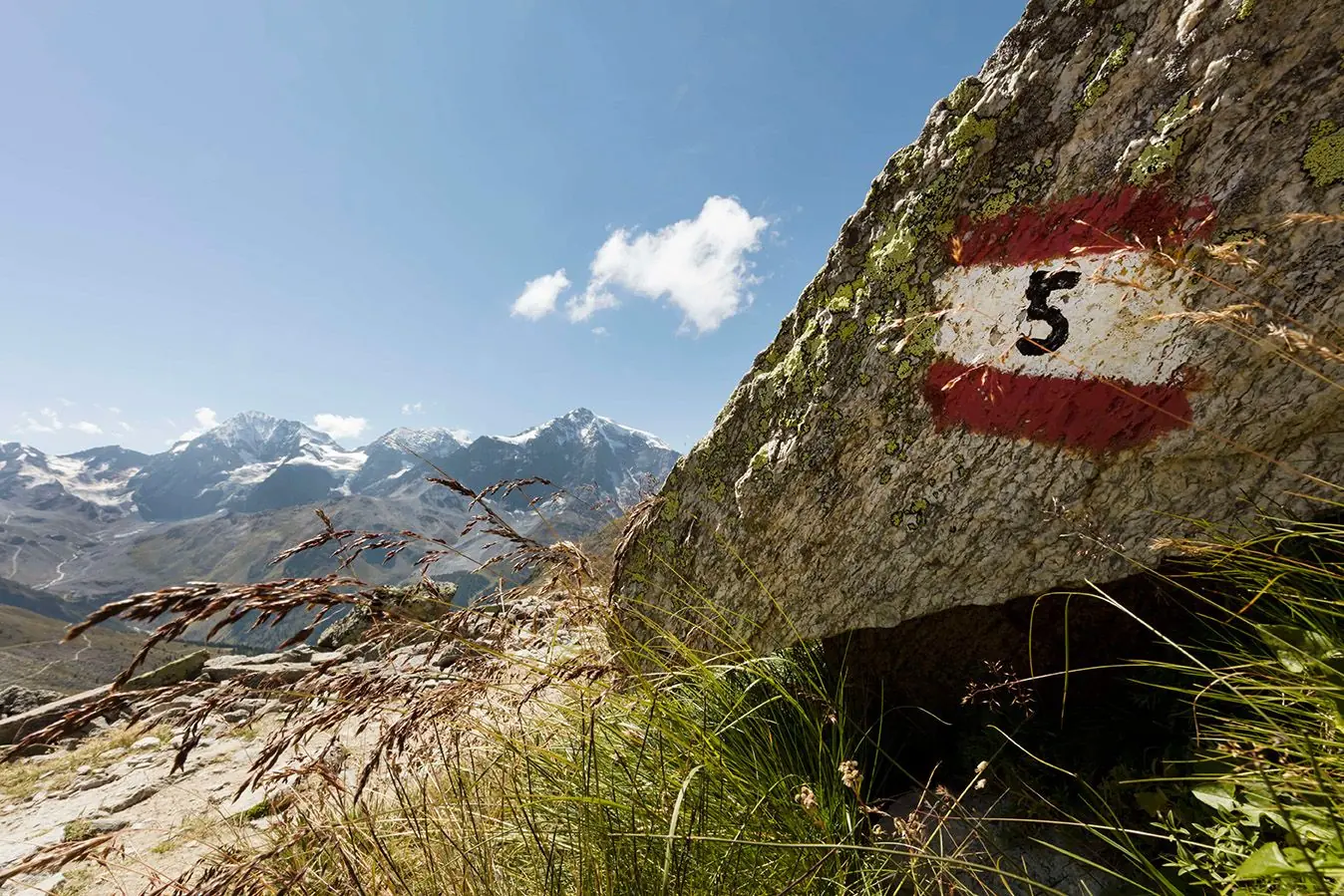Rot-weiße Wegmarkierung auf einem Felsen, dahinter die Gletscher
