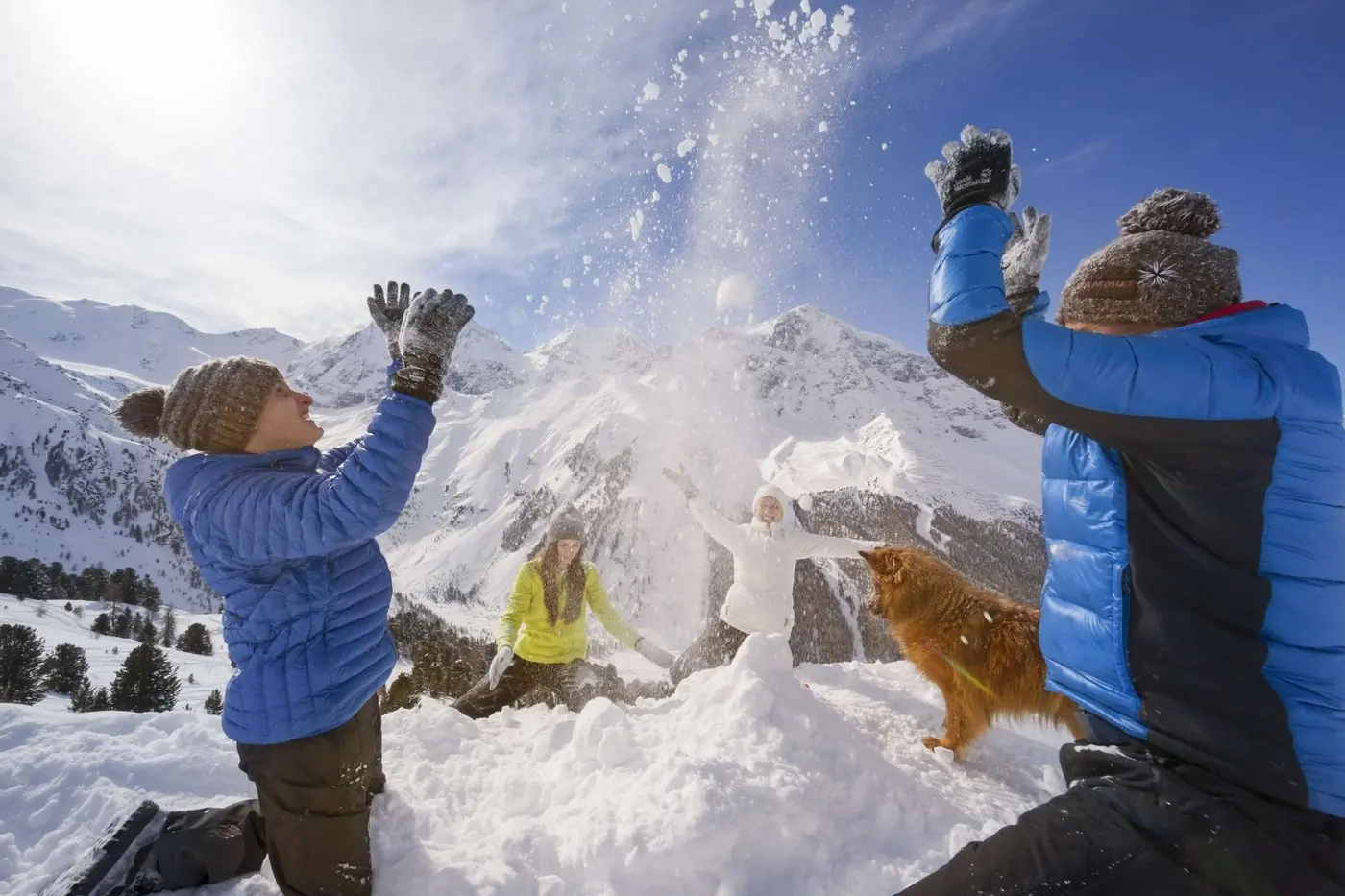 Familie mit Hund bei einer Schneeballschlacht vor den Bergen