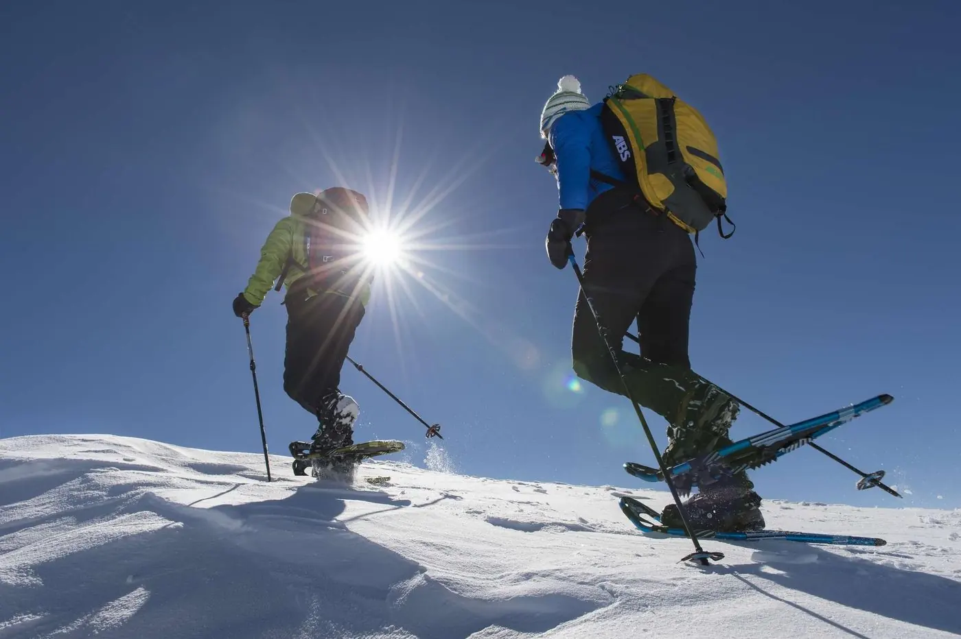Zwei Schneeschuhwanderer im Gegenlicht vor blauem Himmel
